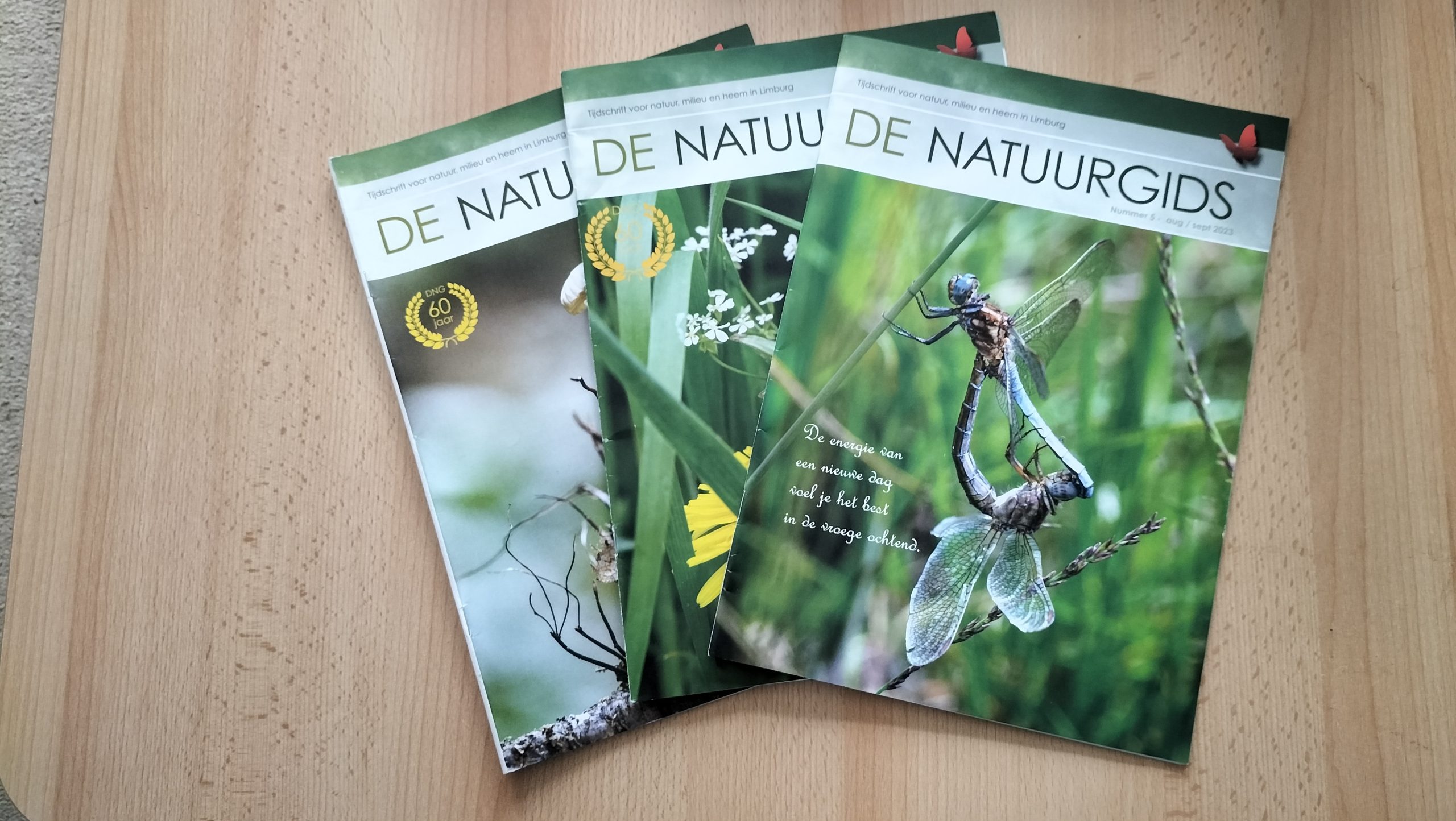 Drie tijdschriften "De Natuurgids" met natuurbeelden op een houten tafel.