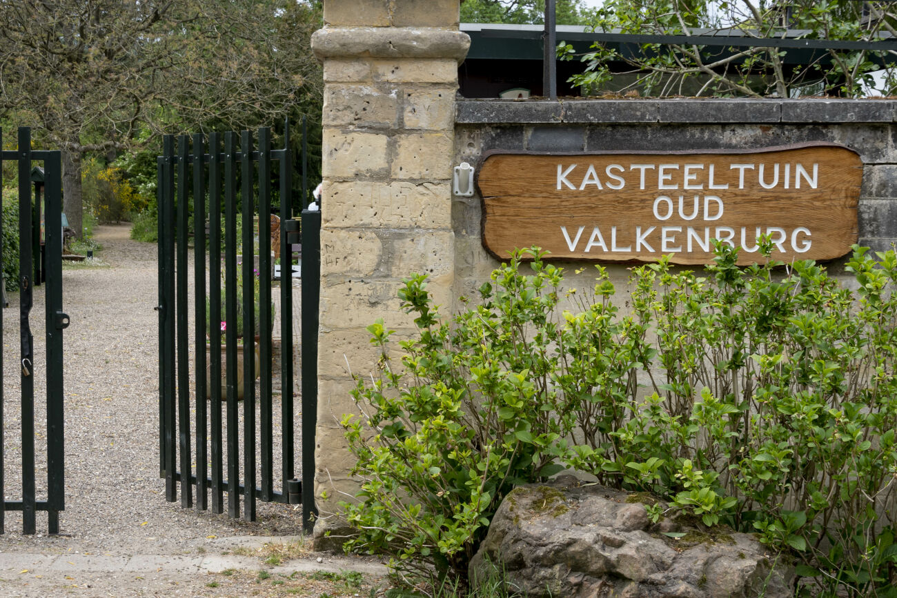 Toegangspoort tot Kasteeltuin Oud Valkenburg met bord en groene struiken.
