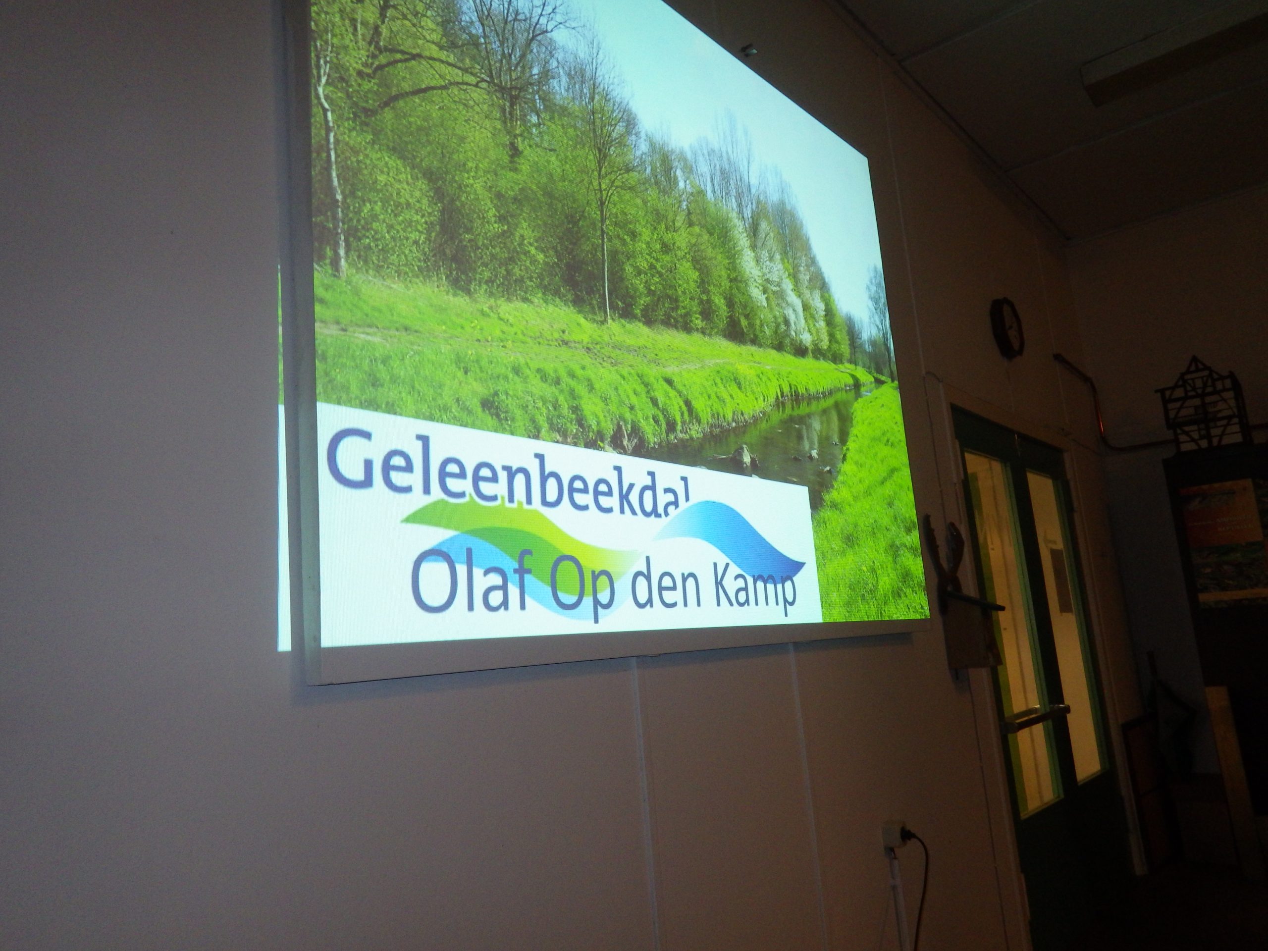 Projectie van een groene vallei met water, tekst "Geleenbeekdal Olaf Op den Kamp".