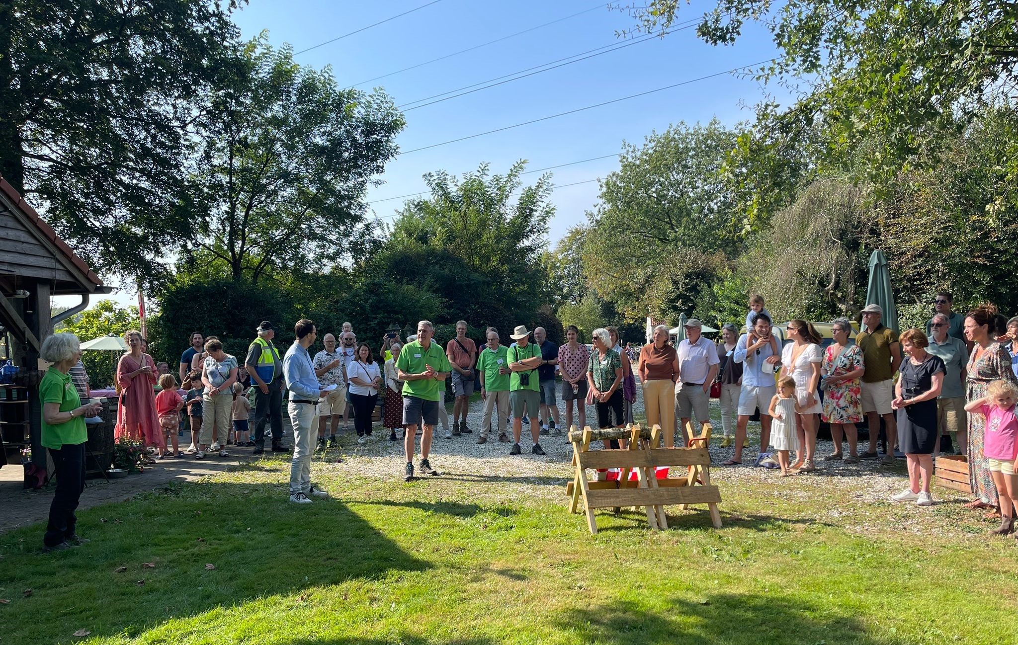 Een groep mensen verzameld in een tuin, luisteren naar een spreker.
