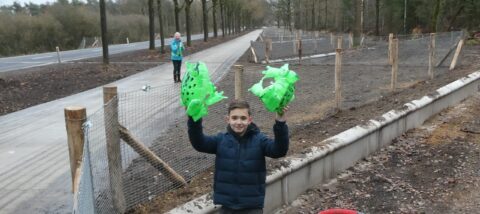 Jongen met groene ballonnen langs een voetpad omheind met gaas, vrouw op achtergrond klapt.