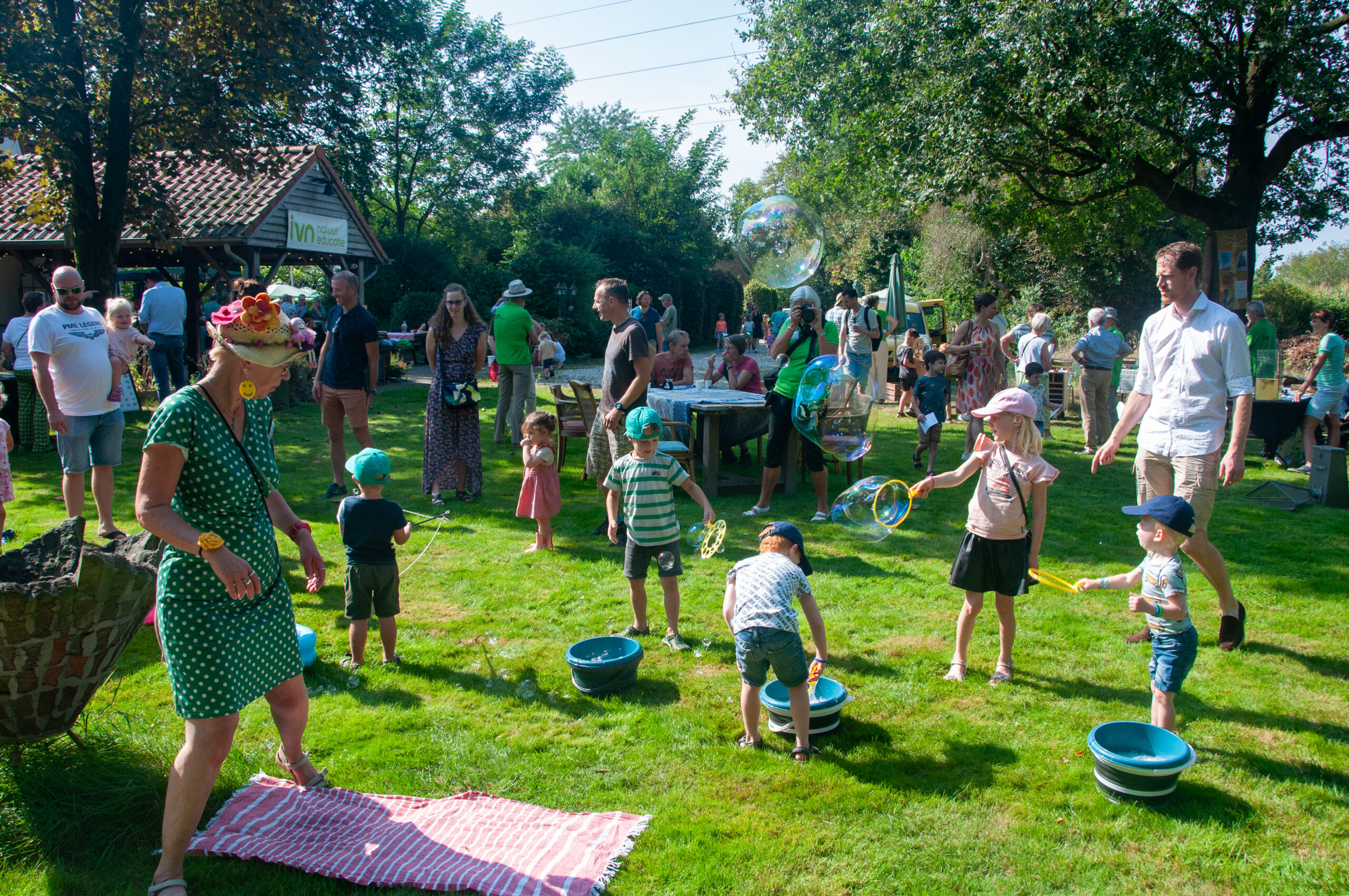 Kinderen maken bellen op grasveld tijdens een drukbezochte buitenbijeenkomst.