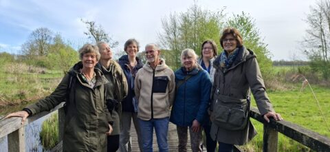 Groep mensen poseert op een brug in een groen, natuurlijk landschap.