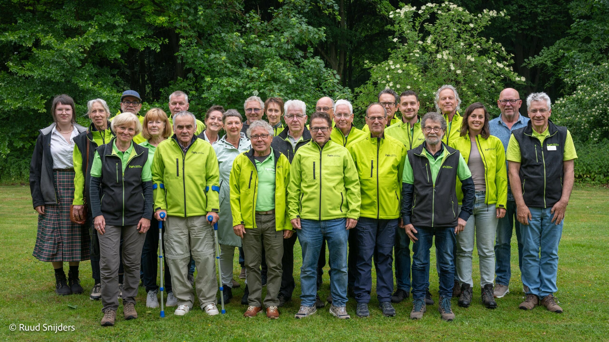 Groepsfoto van mensen in groene jassen in een groene parkachtige omgeving.