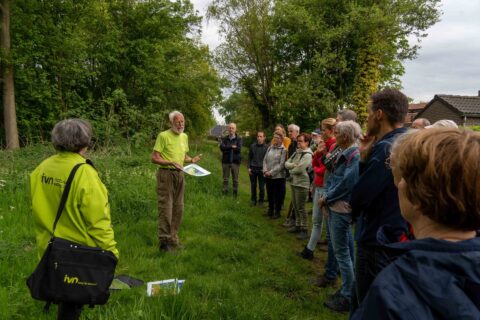 Een man geeft een natuurles aan een groep mensen in een bosrijke omgeving.