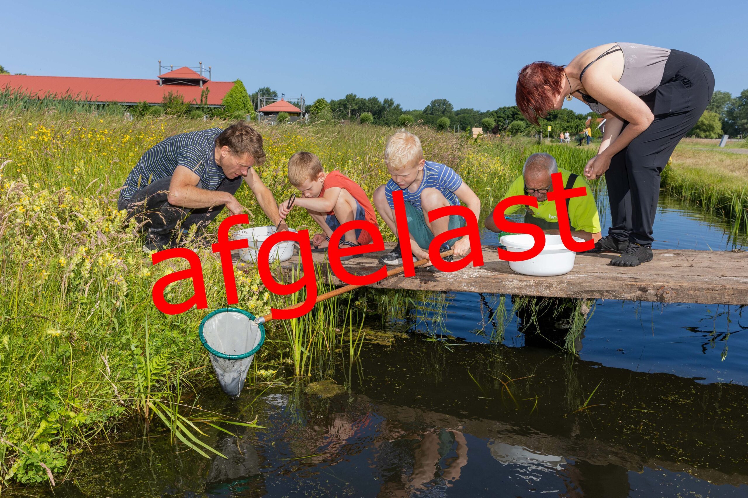 Groepje mensen bij een steiger aan het water; groot rood "afgelast"-tekens.