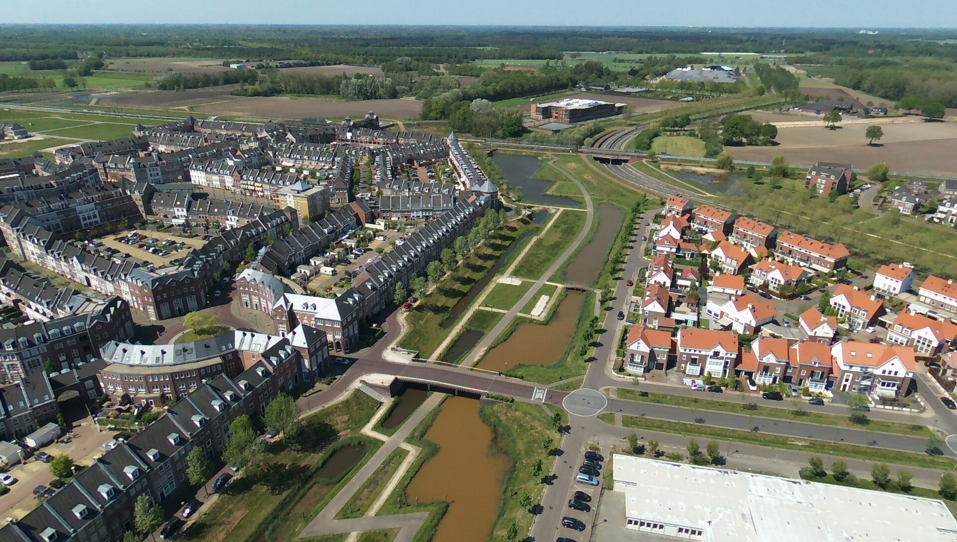 Luchtfoto van een woonwijk met grachten, rijen huizen en omliggende velden.
