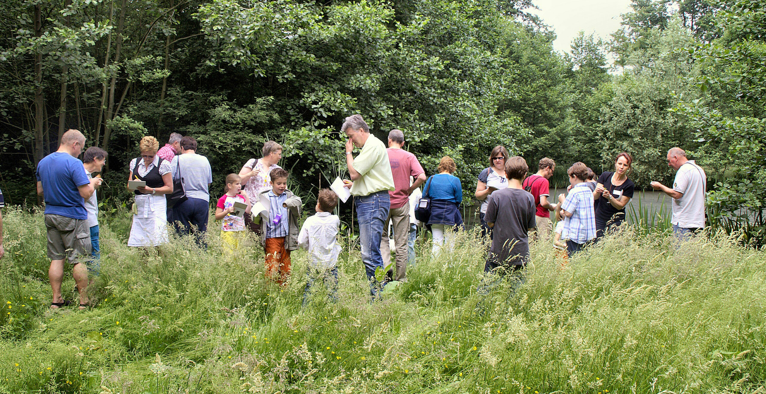 Een groep mensen observeert planten in een groene, bosrijke omgeving.