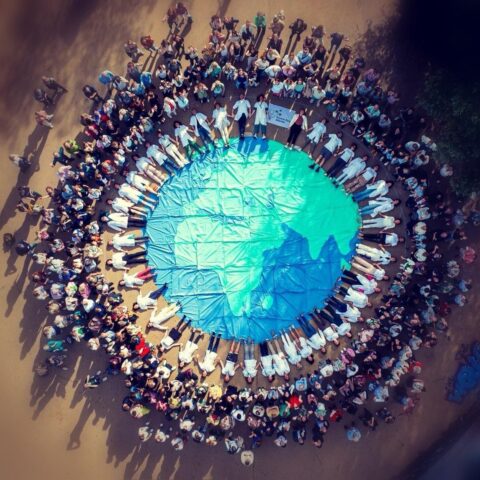 Luchtfoto van mensen in een cirkel rond een groot doek met aarde-afbeelding erop.
