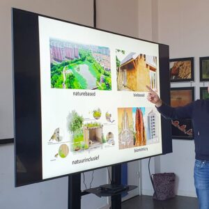 Man geeft presentatie over duurzame ontwerpstrategieën op groot scherm in fotostudio.