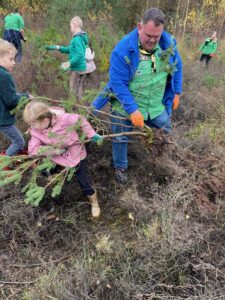 Kinderen en volwassen helpen bij het uitgraven van een kleine boom in een bosgebied.
