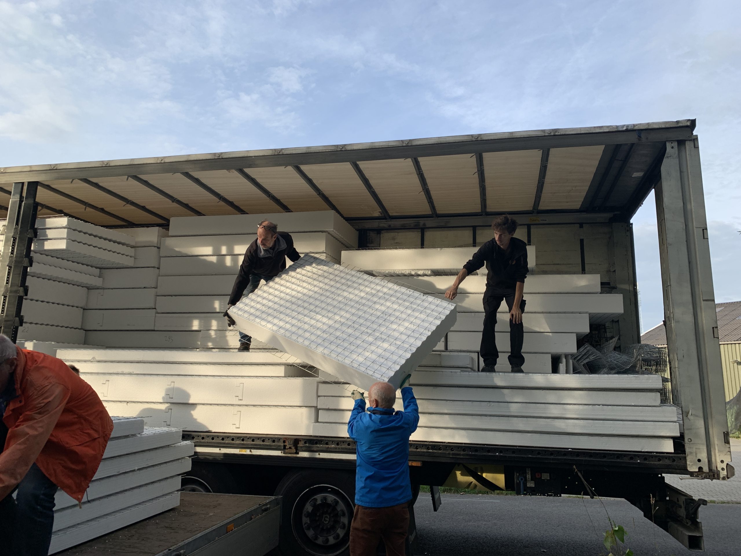 Mensen laden grote, witte platen uit een vrachtwagen op een zonnige dag.