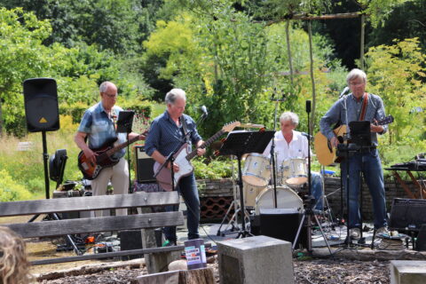 Band speelt live muziek in een groene, buitenomgeving.