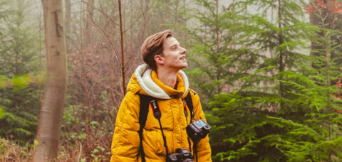 Man in gele jas met camera in mistig bos.