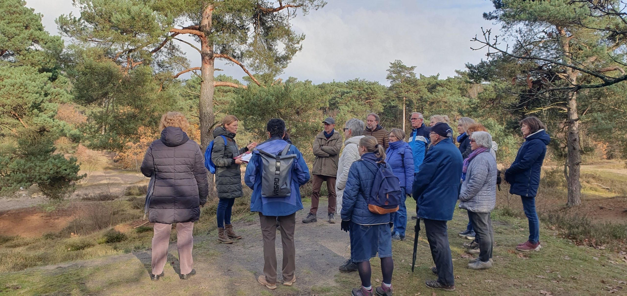 Groep mensen wandelt door een bosrijk gebied onder begeleiding van een gids.