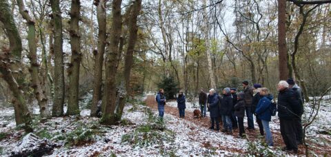 Groep wandelaars in besneeuwd bos luistert naar gids.