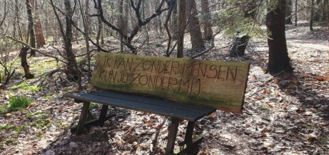 Houten bank in bos met inscriptie: "Ik kan zonder mensen, kun jij zonder mij?"