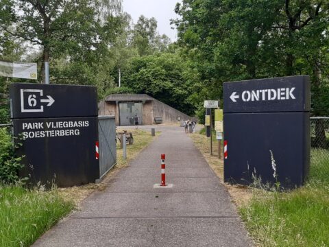 Ingang Park Vliegbasis Soesterberg met borden en pad tussen bomen.
