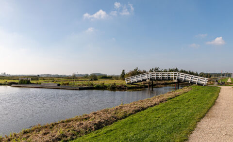 Een wit houten bruggetje over een landelijke sloot met een fietspad en een fiets op de achtergrond.