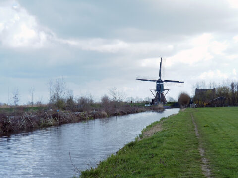 Windmolen naast een kanaal met grasland onder een bewolkte hemel.