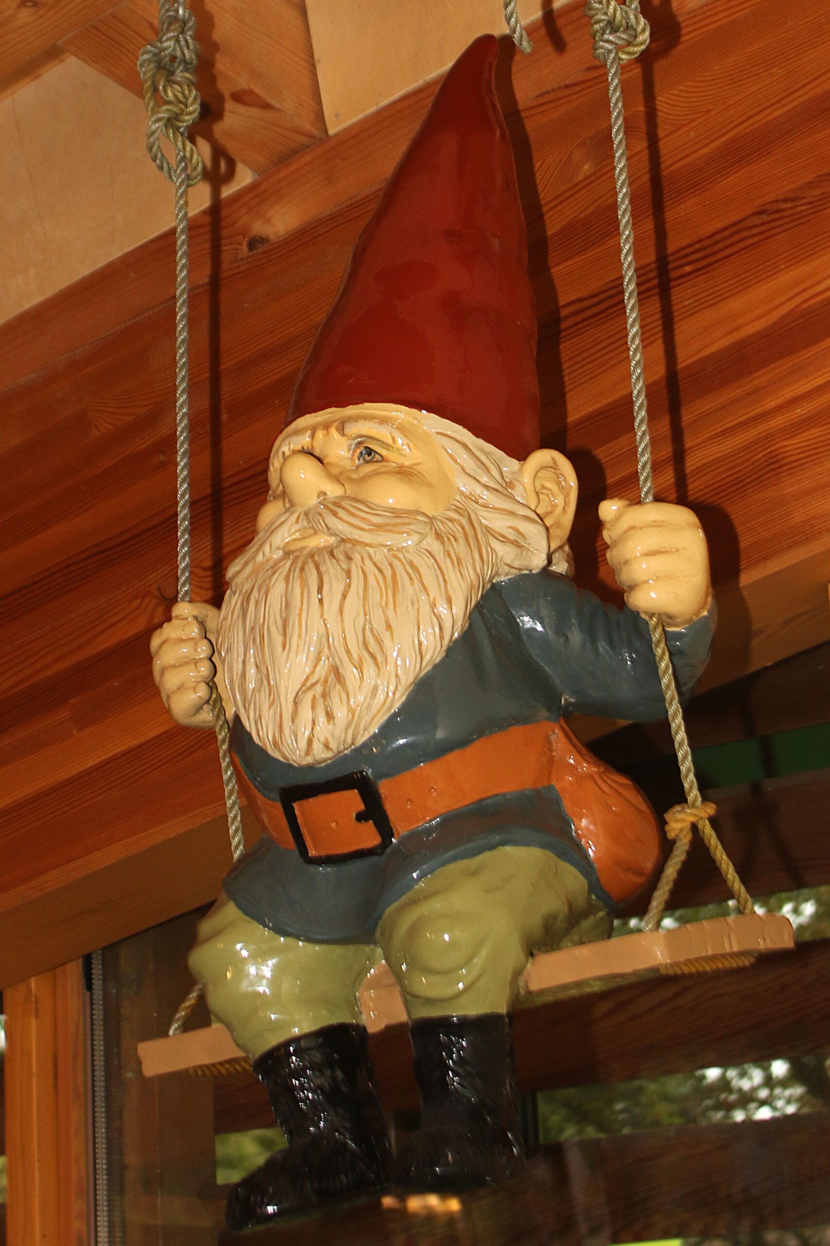 Beeld van tuinkabouter op schommel, hangend aan houten plafond.