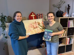 Twee vrouwen poseren met kunstwerken voor een boekenplank.
