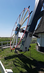 Witte wiek van een windmolen tegen blauwe lucht, met grasveld en hek eromheen.