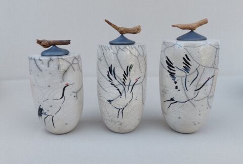 Drie keramische potten met kraandecoraties en deksels van hout en steen.