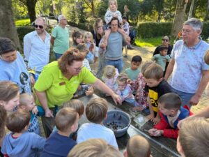 Een groep mensen verzameld rond een tafel met een kom vol slakken, in een parkachtige omgeving.