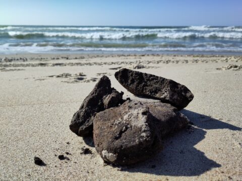 Stenen op zandstrand met zee en golven op de achtergrond onder een heldere blauwe hemel.