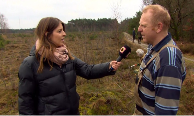 Een journalist interviewt een man in een natuurgebied met een microfoon.