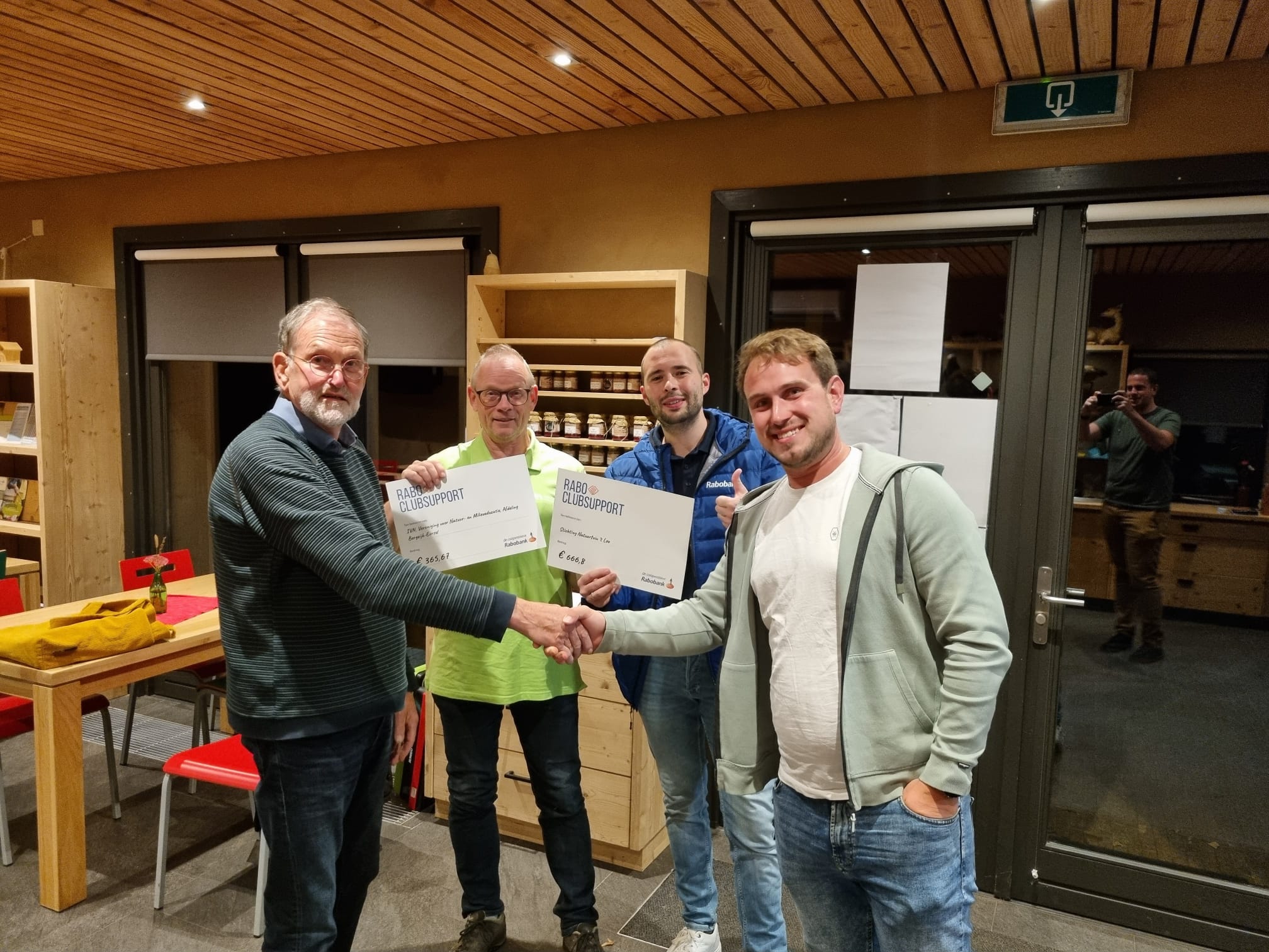 Vier mannen poseren met certificaten in een houten interieur.