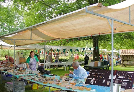 Marktkraam met handgemaakte spullen, kleurrijke vlaggetjes, en mensen in een parkachtige omgeving.