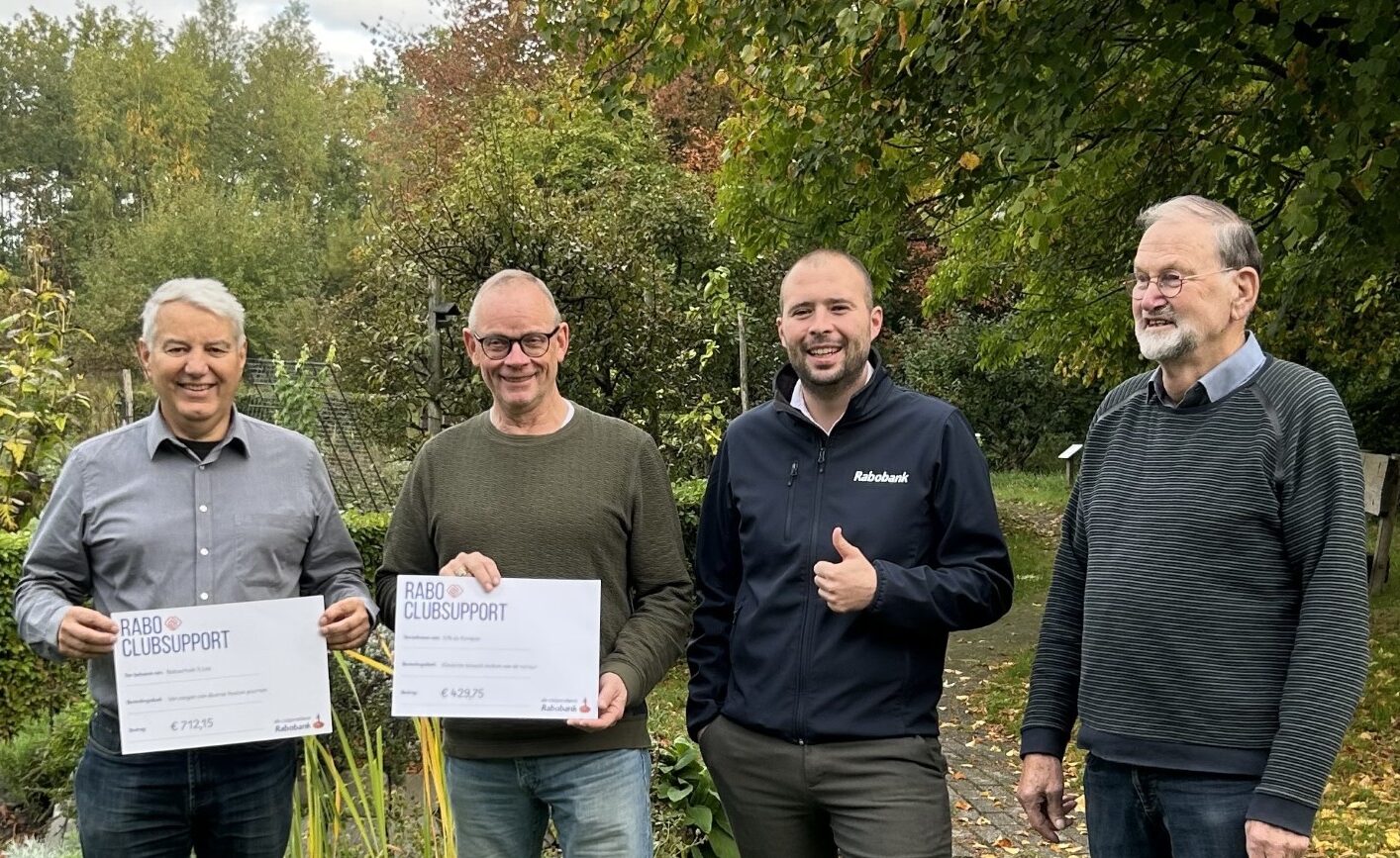 Vier mannen poseren buiten met Rabo ClubSupport cheques, omringd door bomen.