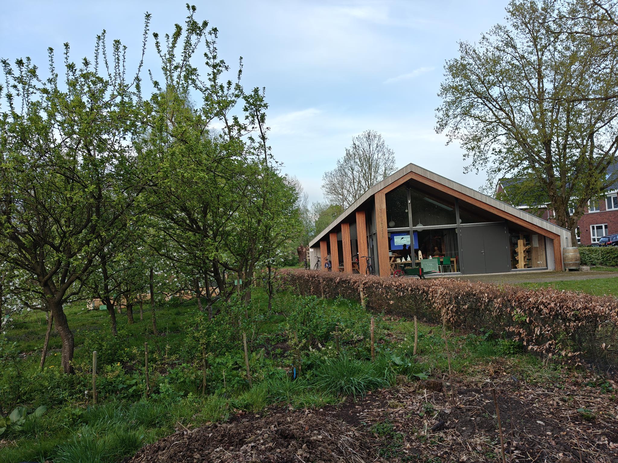 Modern gebouw in groene omgeving met bomen, struiken en een heldere hemel.