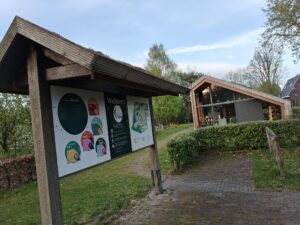 Infobord bij tuin; modern gebouw op achtergrond, omgeven door groen.