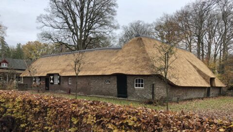 Een traditionele boerderij met rieten dak, omringd door herfstbomen en bladeren.