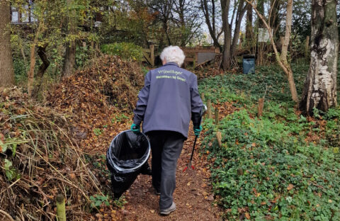 Vrijwilliger ruimt afval op in bosrijk gebied met grijper en vuilniszak.