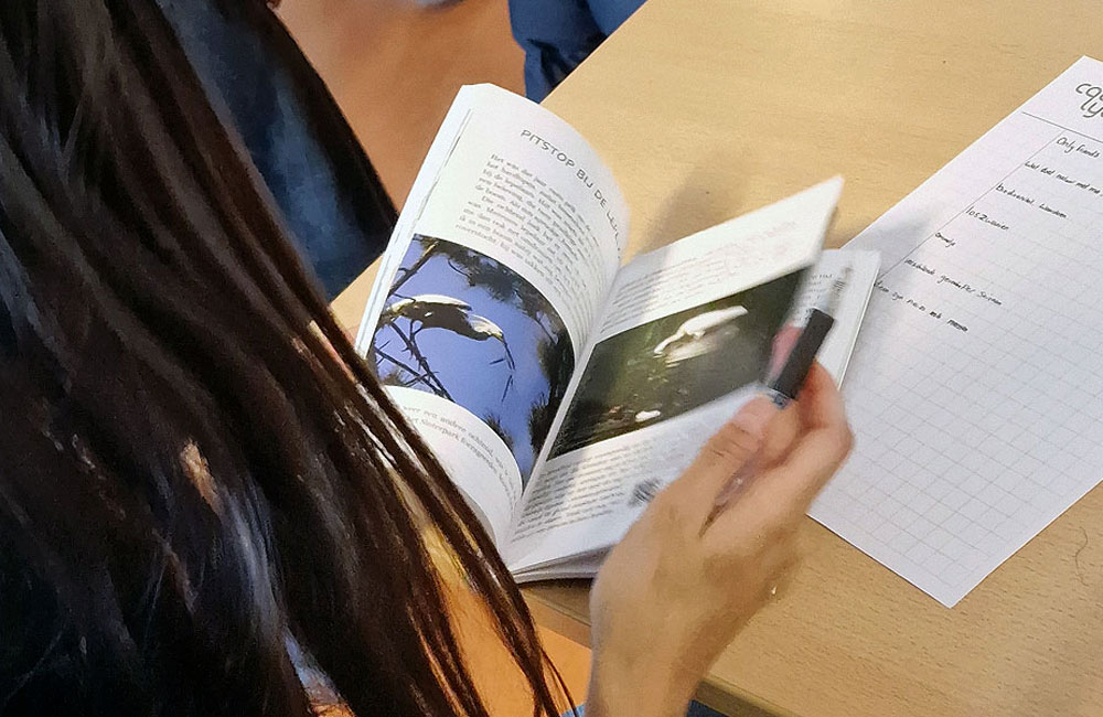 Persoon leest boek met vogelfoto's aan tafel, naast notities op een ruitjespapier.