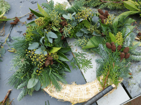 Groene kerstkrans met dennenappels en bladeren op een grijze stenen ondergrond.
