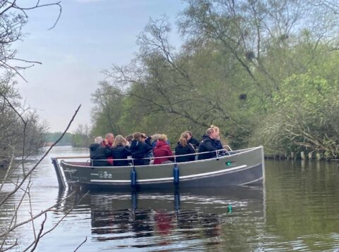 Een boot vol mensen vaart rustig door een kanaal, omgeven door groene bomen.