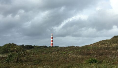 Rode en witte vuurtoren steekt uit boven duinlandschap onder bewolkte hemel.