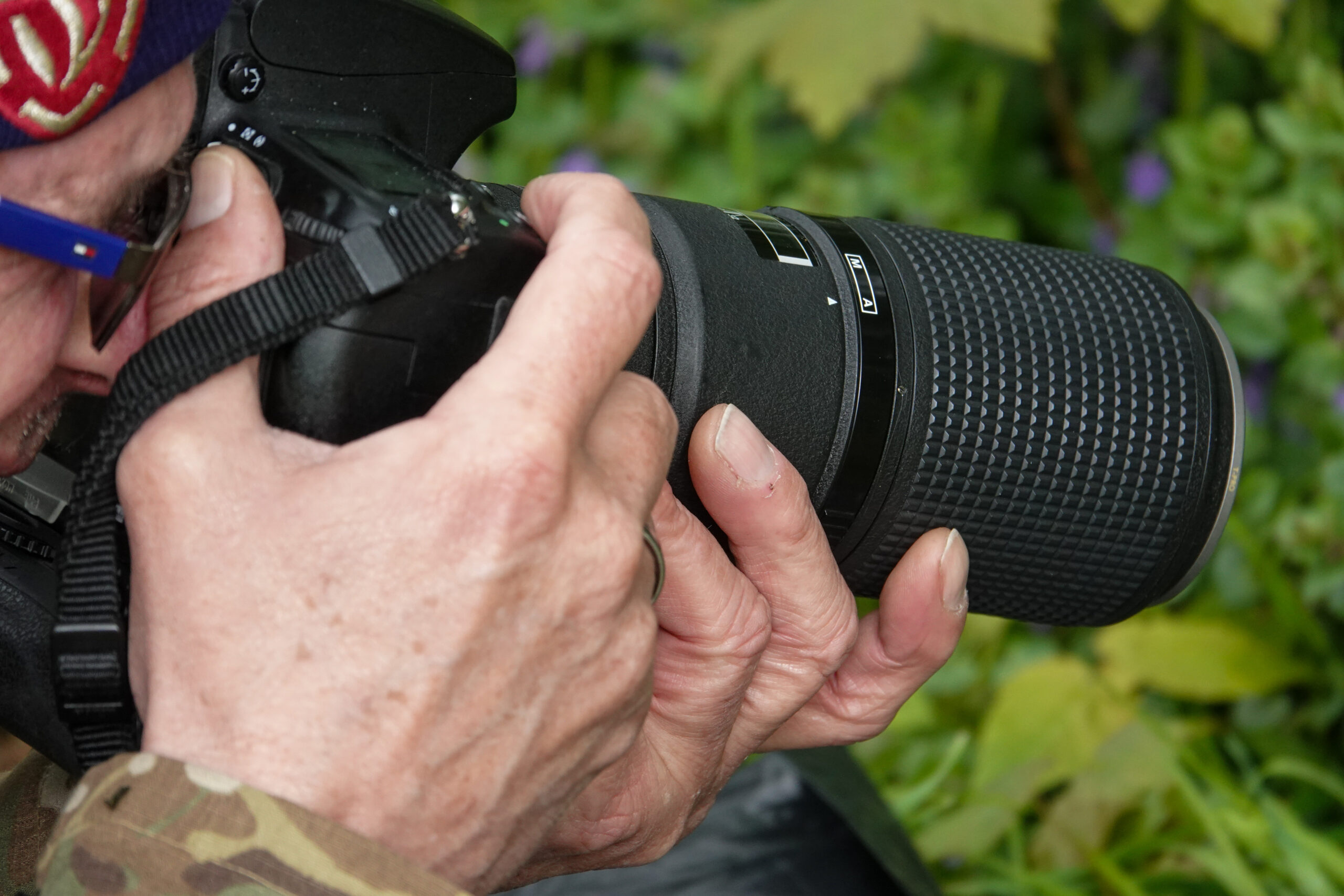 Persoon houdt een camera met telelens vast, gereed om een foto te maken in een groene omgeving.