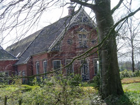 Rood bakstenen huis met decoratieve gevel, omgeven door bladloze bomen en een groene tuin.