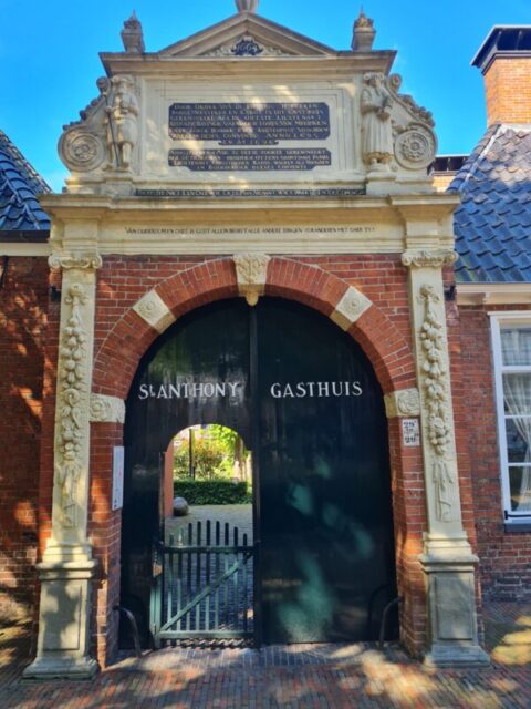Historische poort van St. Anthony Gasthuis, rode baksteen en sierlijke details, doorgang zichtbaar.