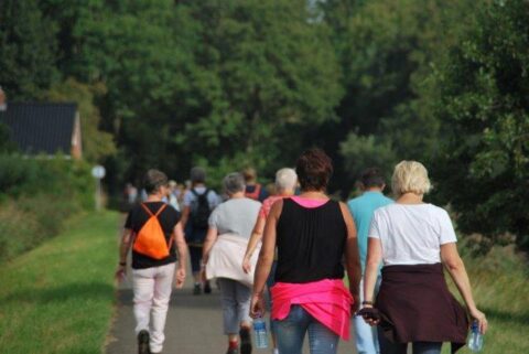 Een groep mensen wandelt op een landweg, omgeven door groene bomen.