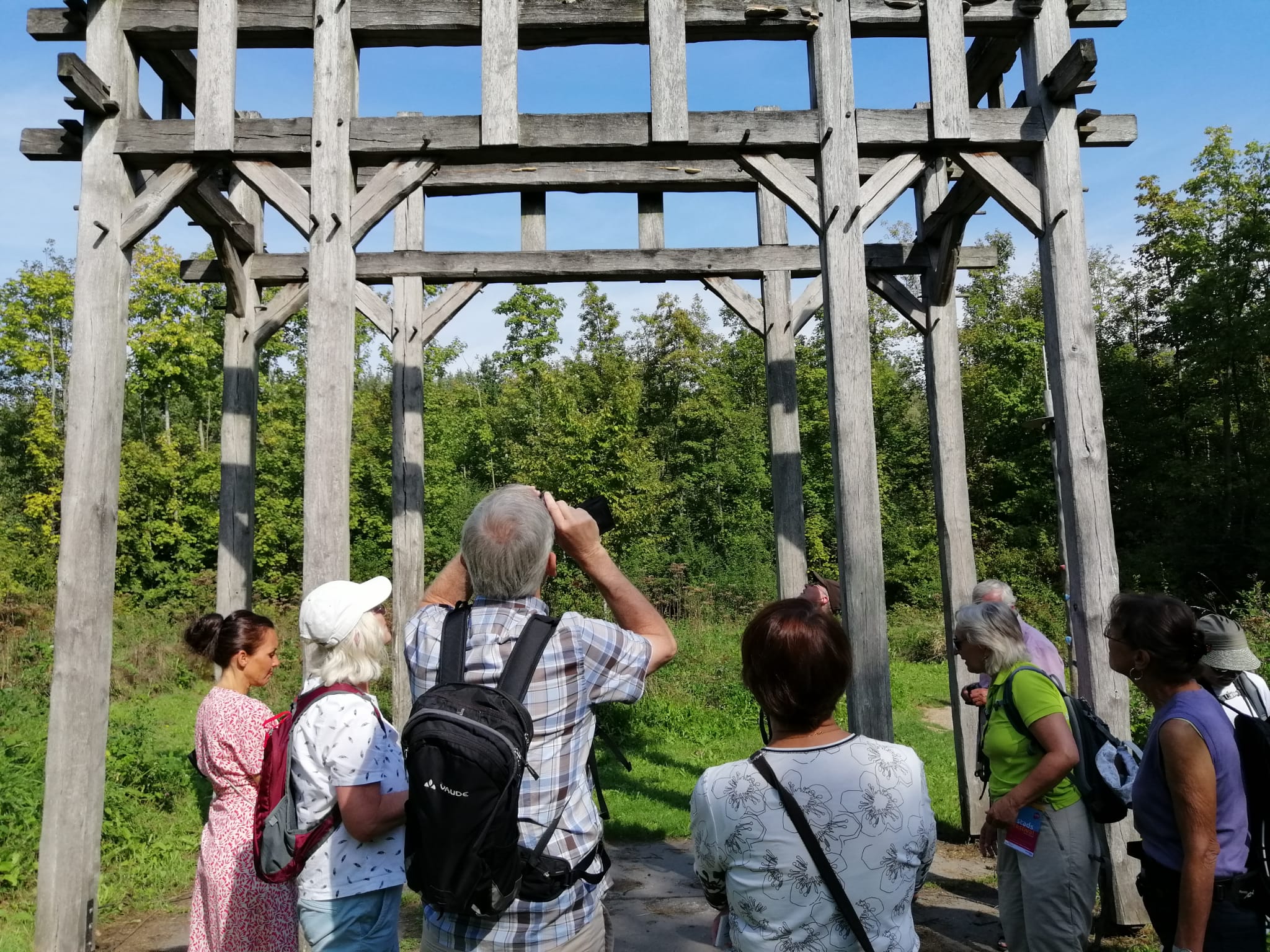 Groep mensen bekijkt houten constructie in een bosrijke omgeving.