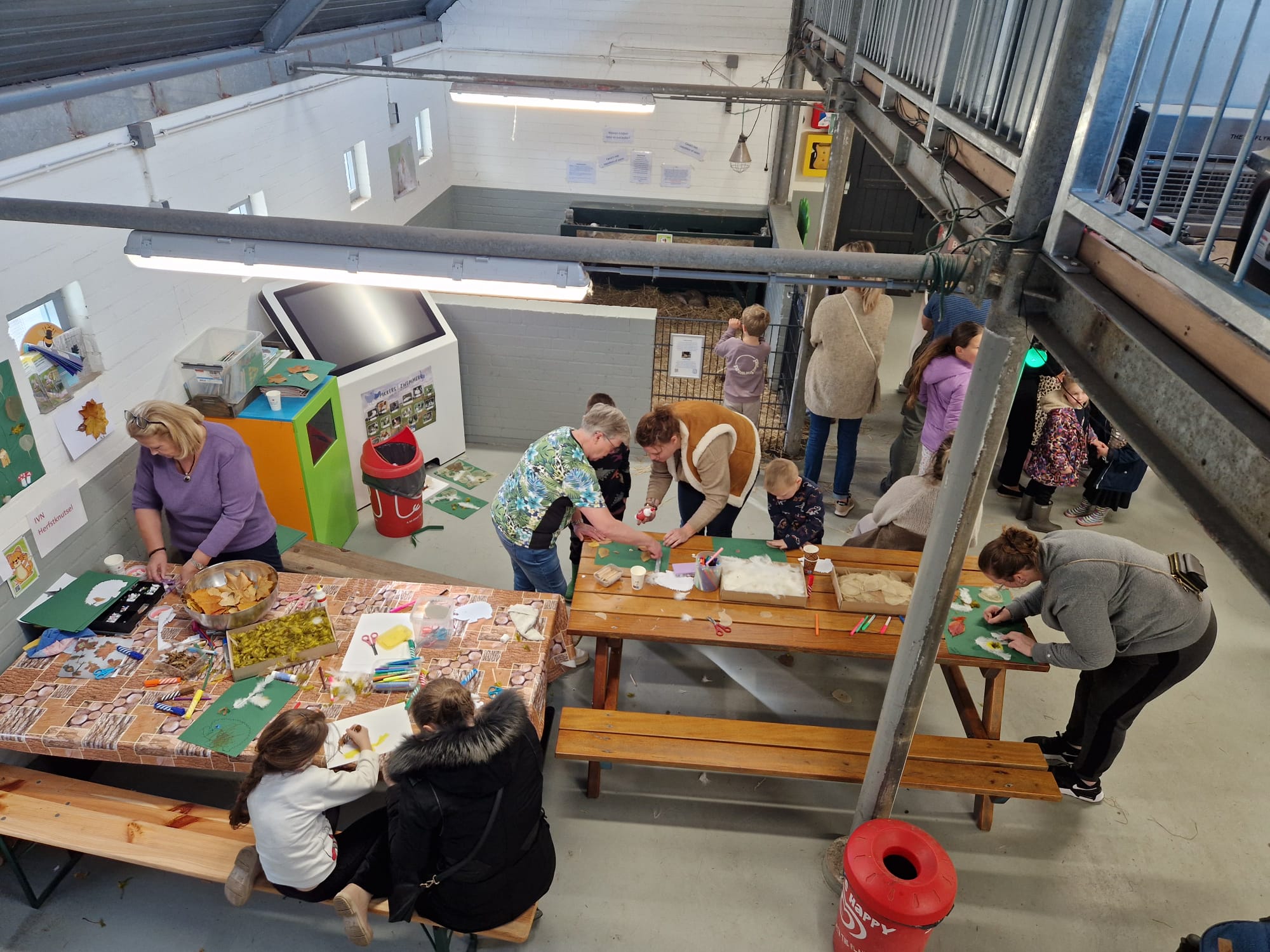Kinderen en volwassenen knutselen samen aan tafels in een creatieve workshopruimte.