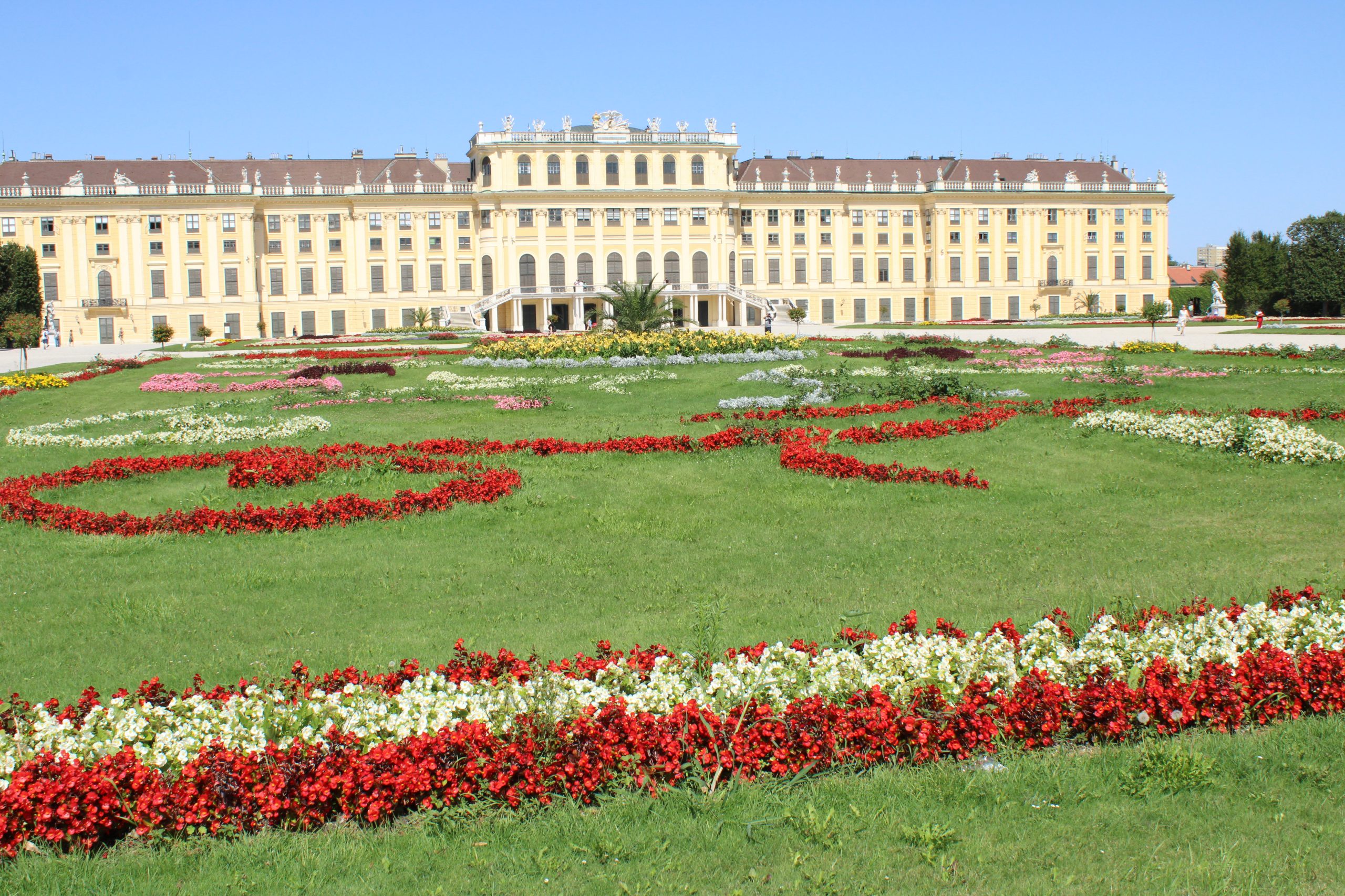 Groot paleis met sierlijke bloembedden en gazon op een zonnige dag.
