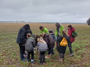Een groep mensen buigt zich over grasland onder een grijze, bewolkte hemel.